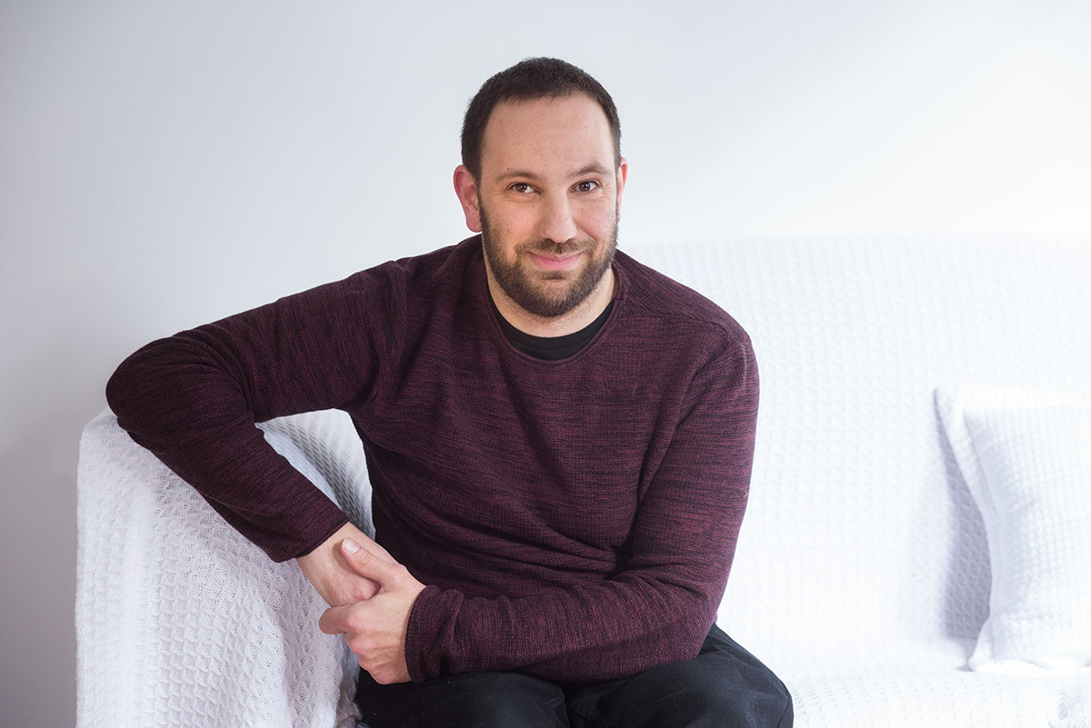 Digital accessibility expert Adem Cifcioglu is sitting on a white couch and looking at the camera.