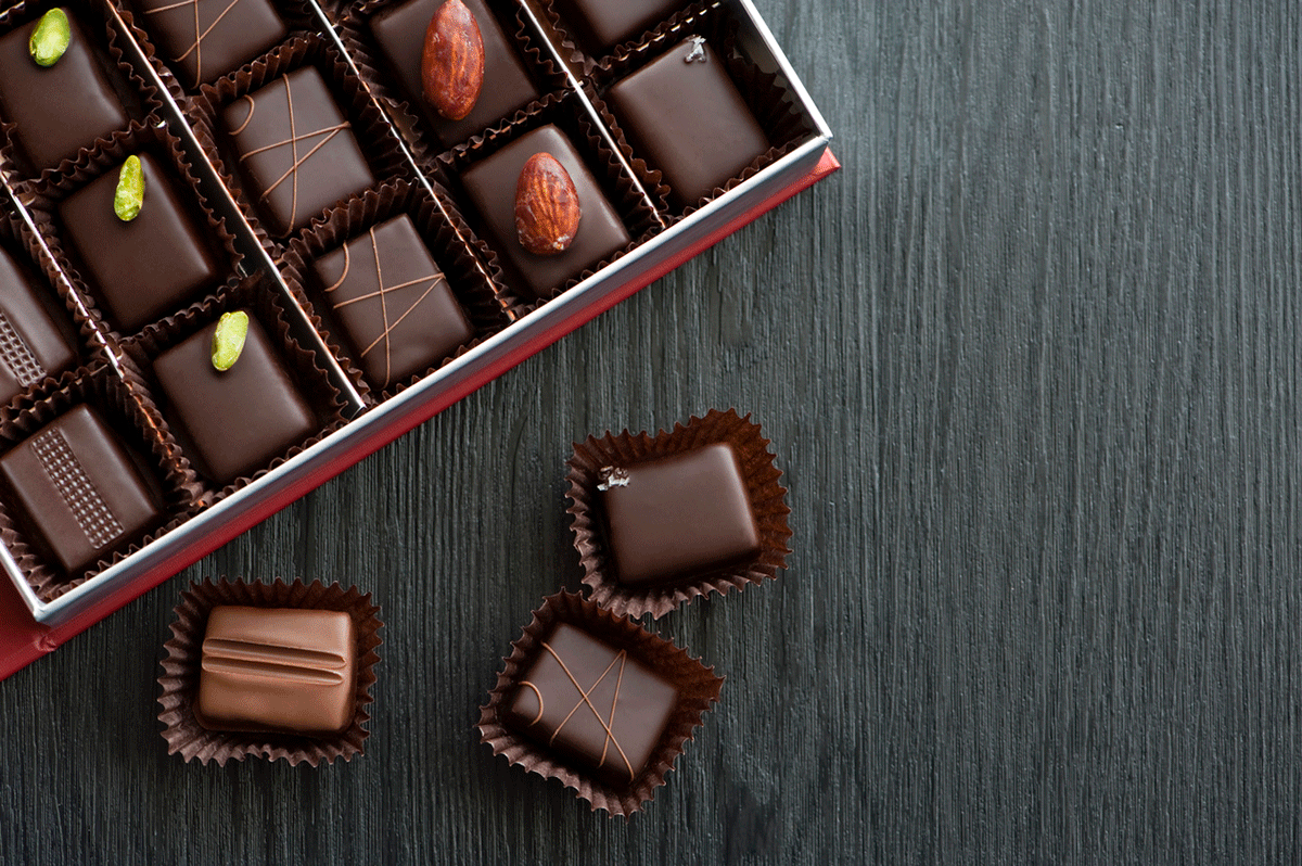 A box of fancy chocolates, with a few chocolates sitting outside the box.