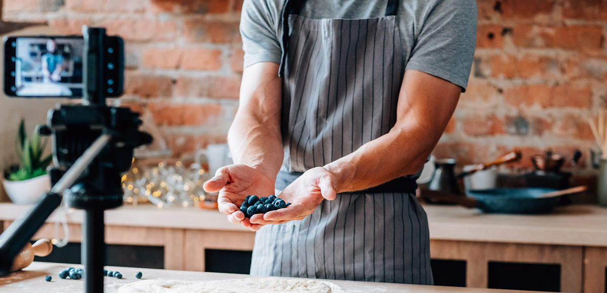 A chef holding berries in front of a phone that is filming him