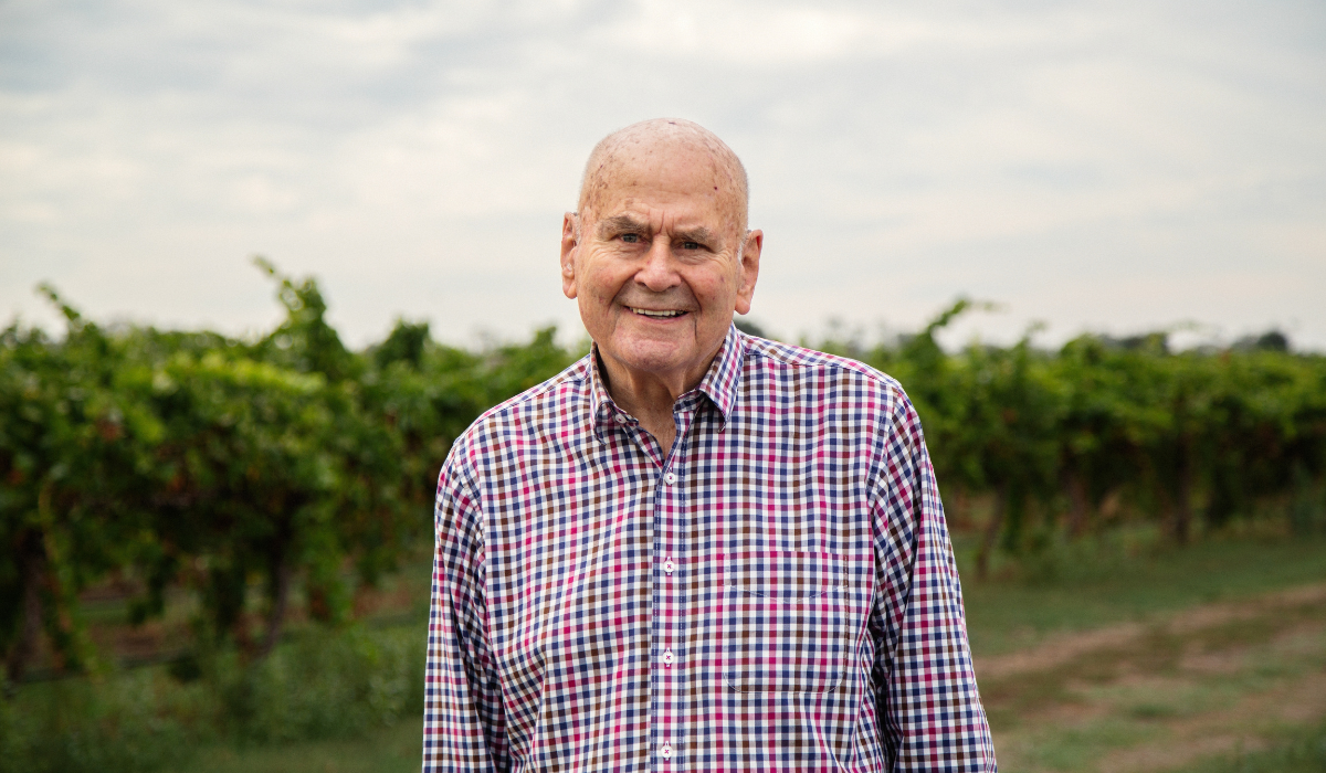 A man stands in front of a vineyard