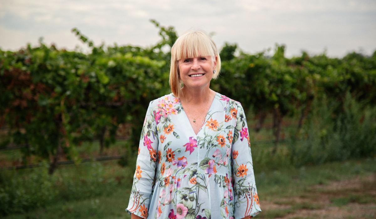 A woman stands in front of a vineyard