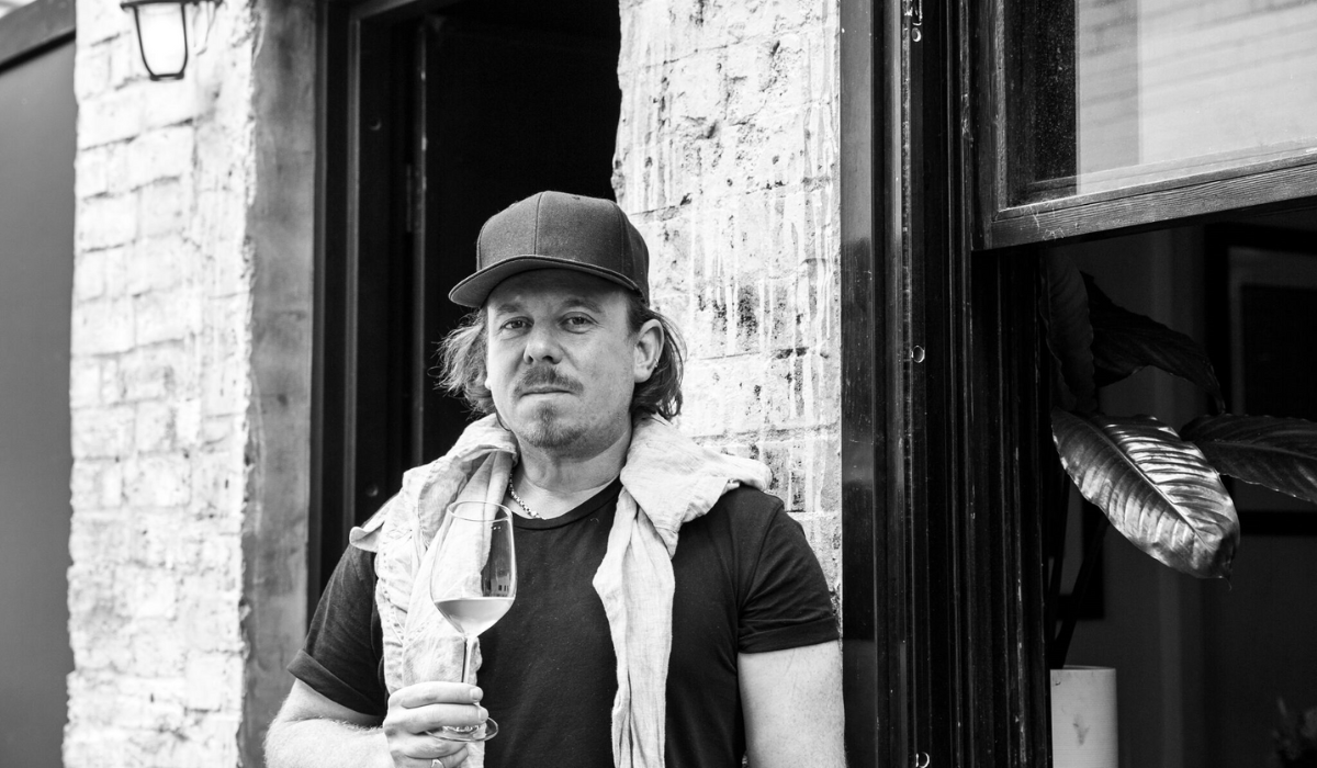 A man stands in front of a building holding a glass of wine