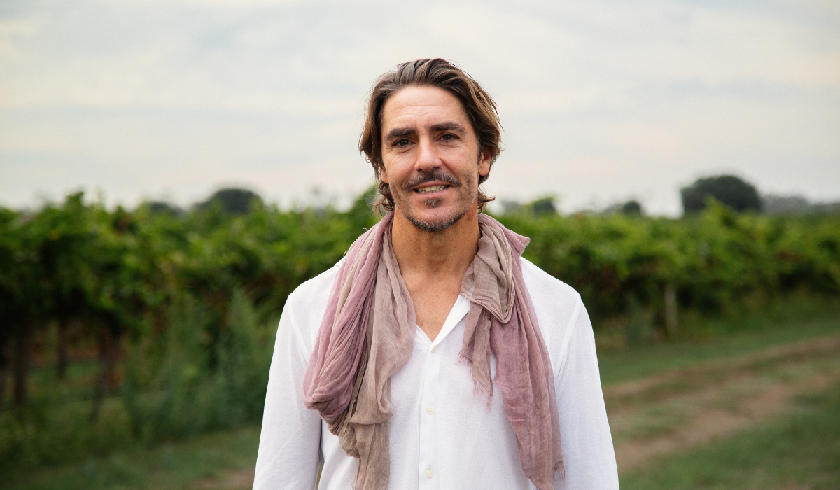 A man poses in front of a vineyard