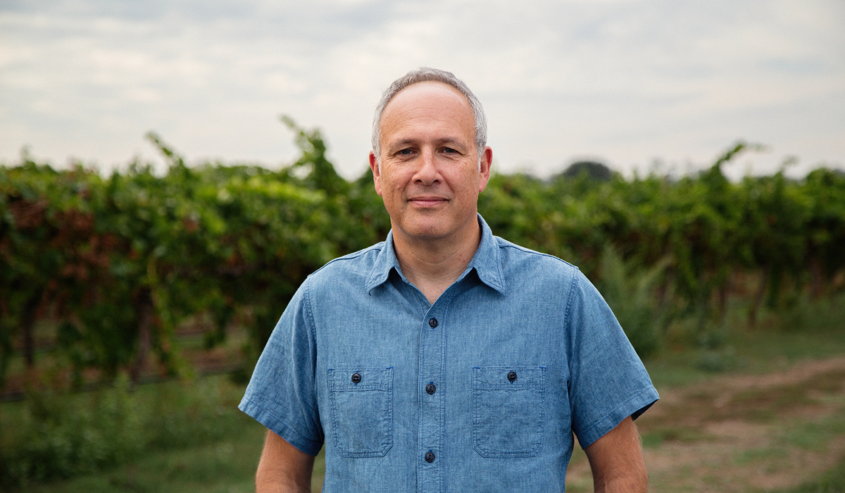 A man poses in front of a vineyard