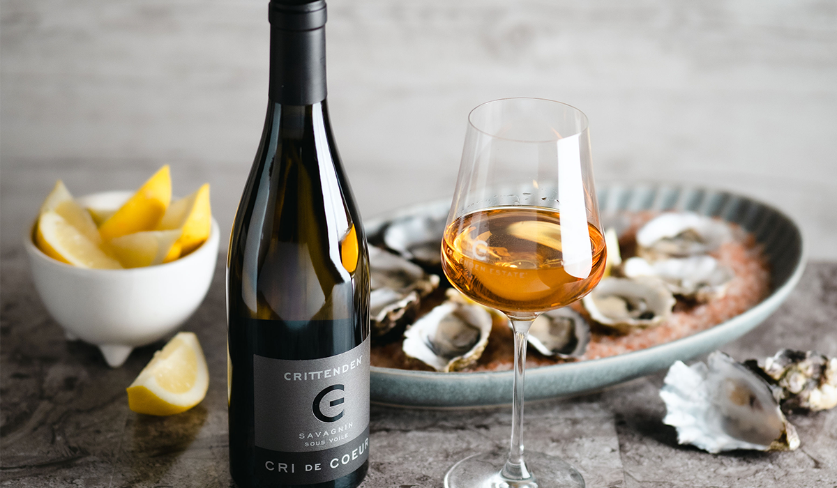 A bottle of Cri de Coeur with a poured glass, surrounded by oysters and wedges of lemon