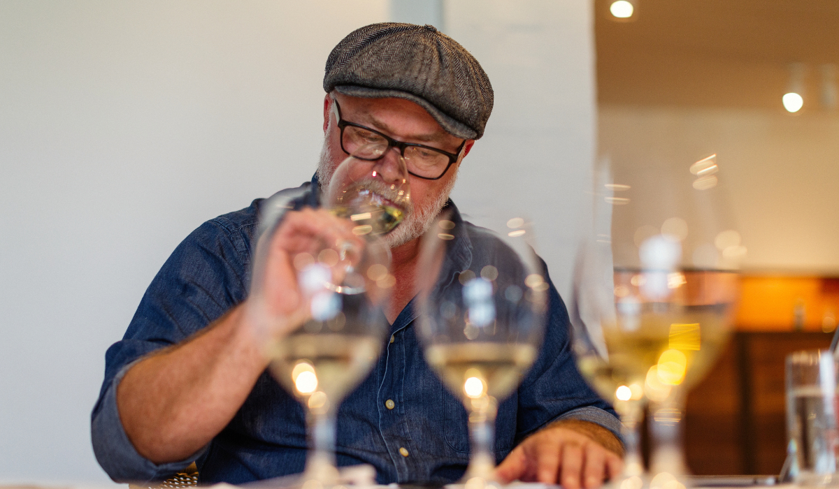 A man wearing a hat sniffs a wine glass