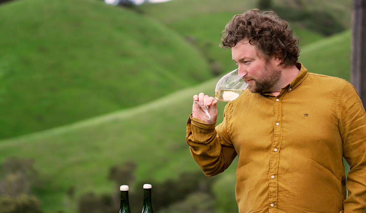 Patrick Sullivan in a mustard shirt smelling a glass of white wine.
