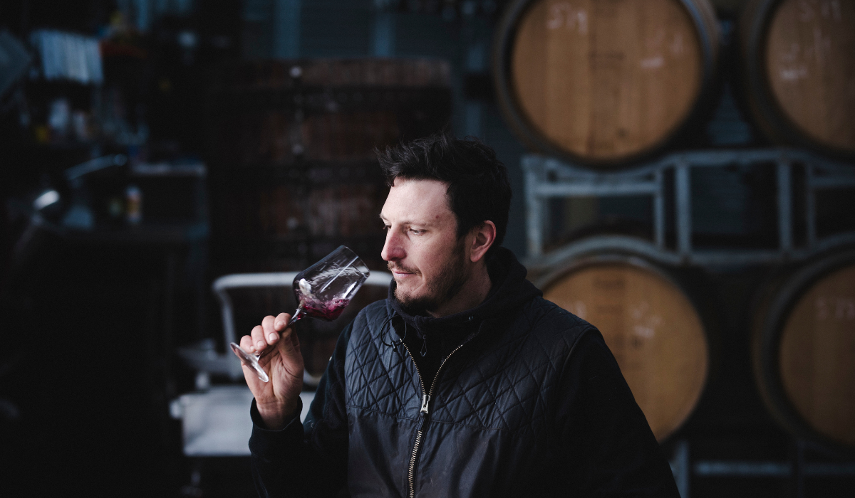 a male winemaker smells a glass of wine in a barrel room