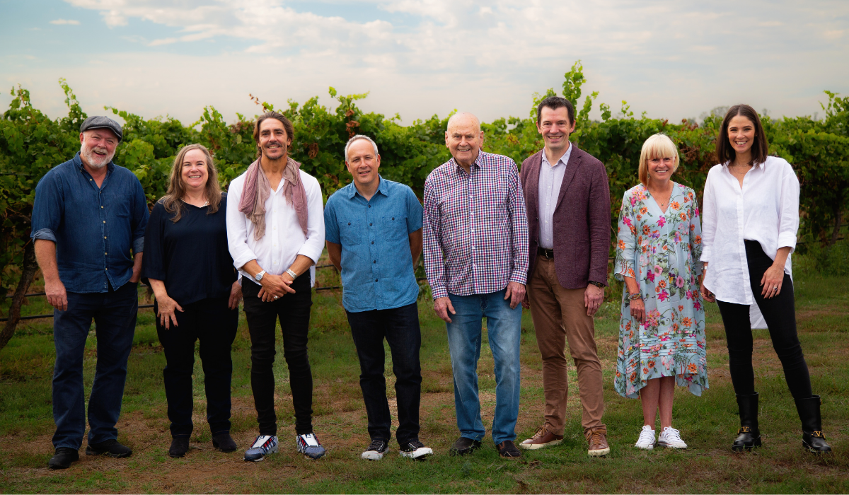 Eight men and women stand in front of grape vines