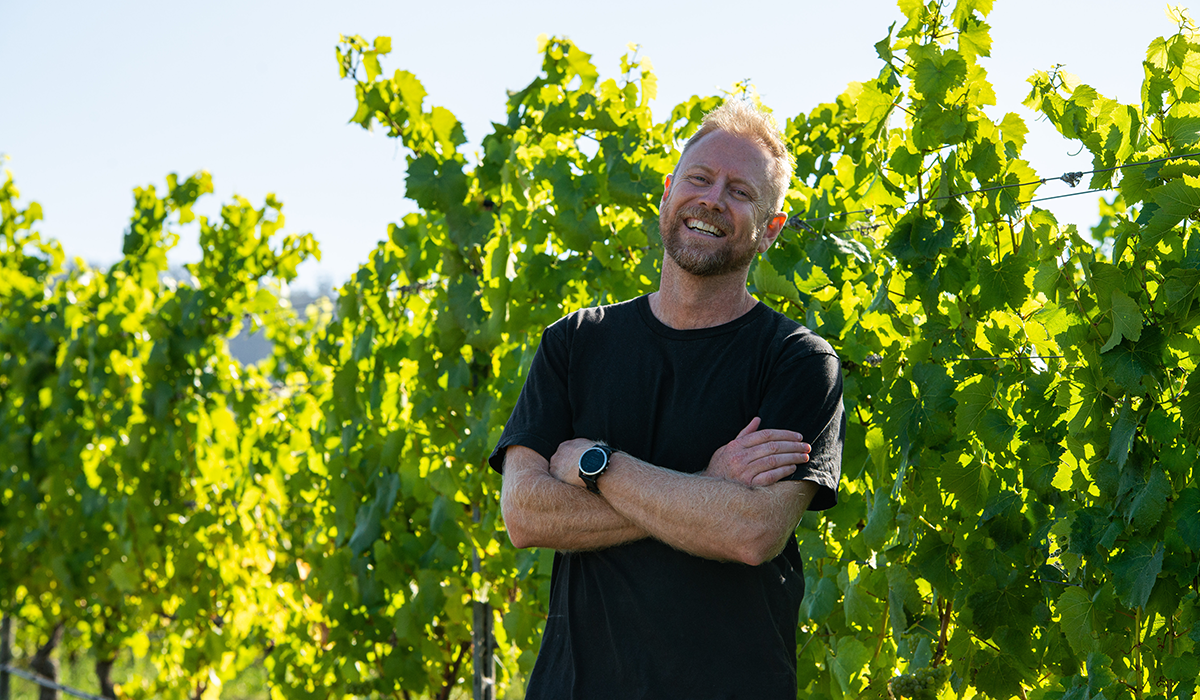 Adam Wadewitz in the vineyard with his arms crossed and laughing