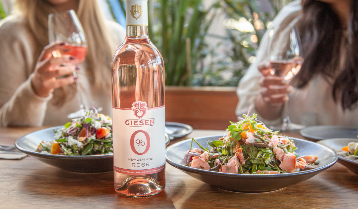 A bottle of rose wine on a table in front of two women eating salads