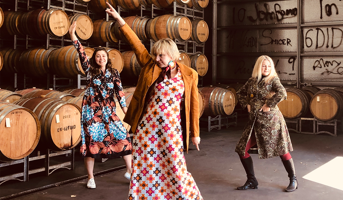 Three women strike a pose in front of wine barrels