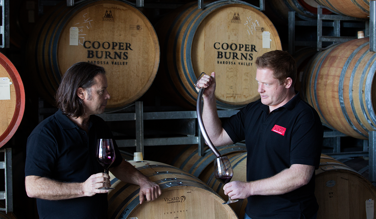 Two men testing wine from a barrel