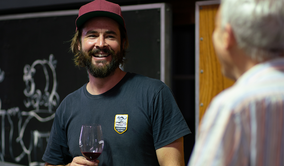 Nick Dugmore in a maroon hat holding a glass of red wine