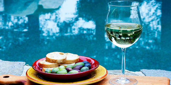 Glass of wine and bowl of olives by pool