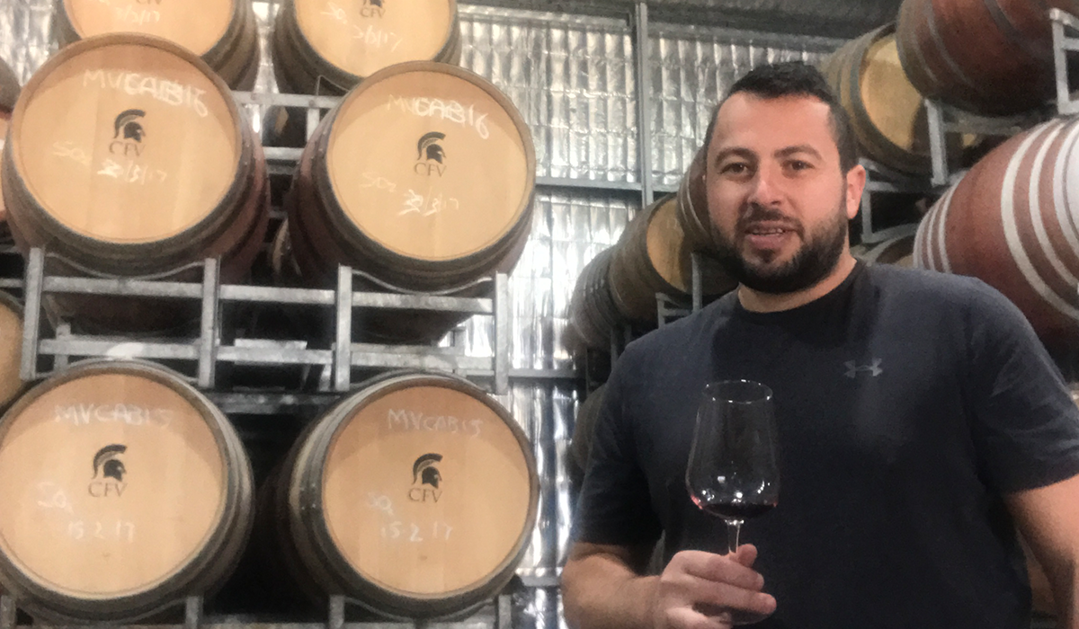 Mark with wine barrels holding a glass of grenache