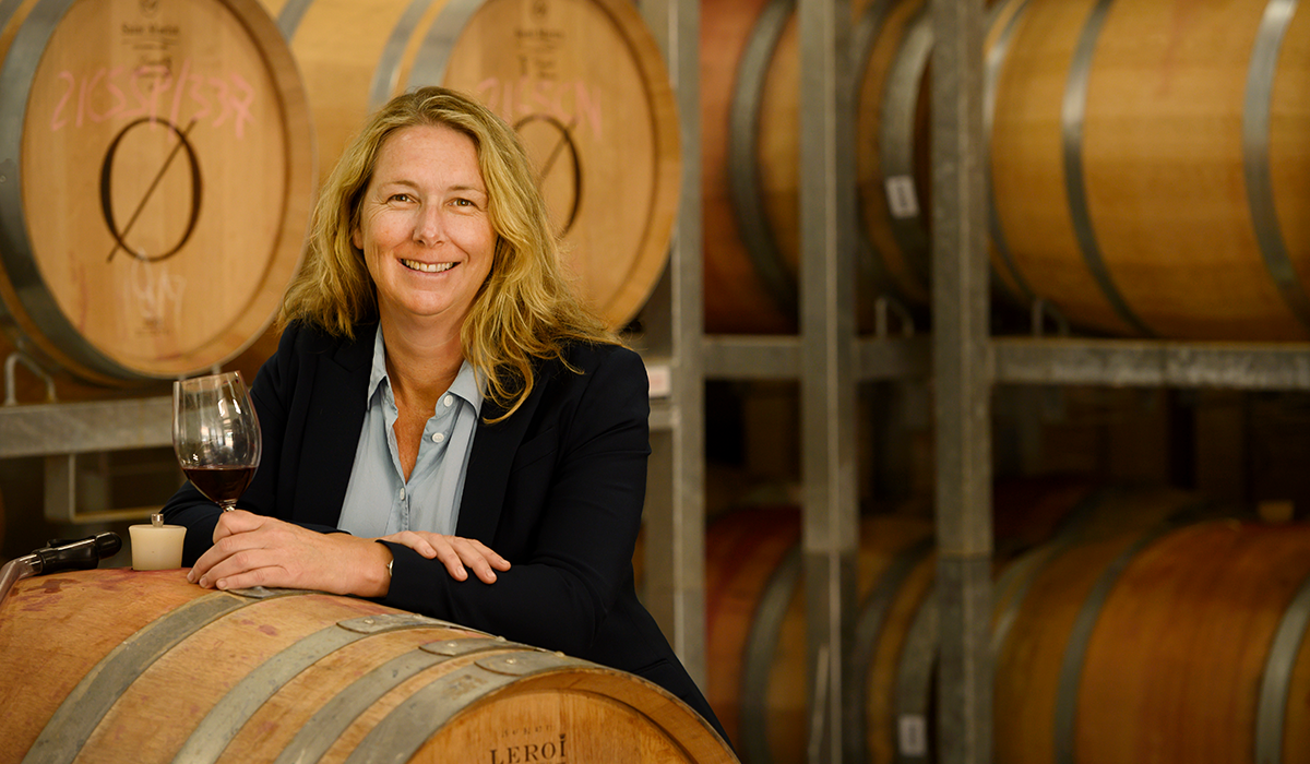 Cath Oates in the barrels holding a glass of red wine