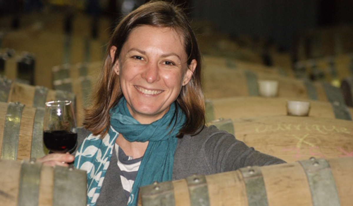 Vanessa Carson holding up a glass of wine in between the barrels