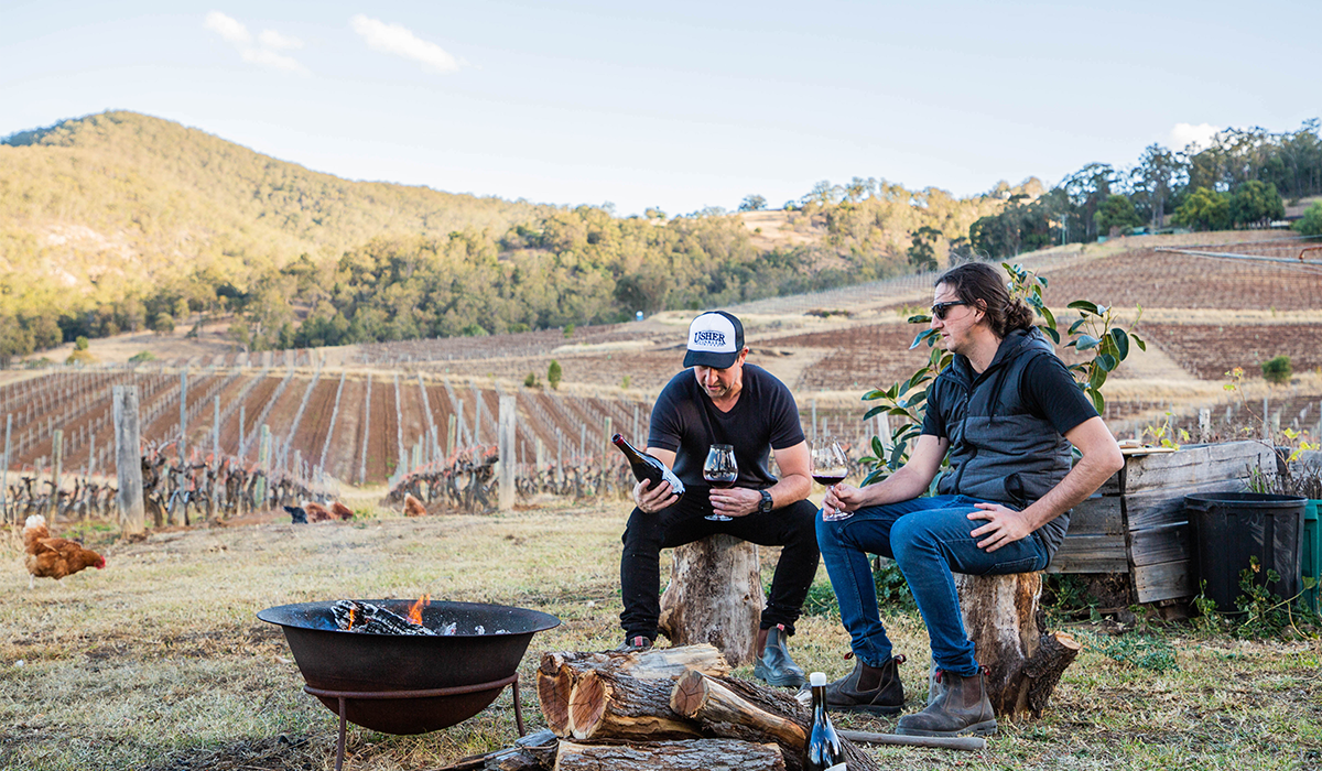 Usher Tinkler and winemaker enjoying a wine by the fire with the vineyard in the background
