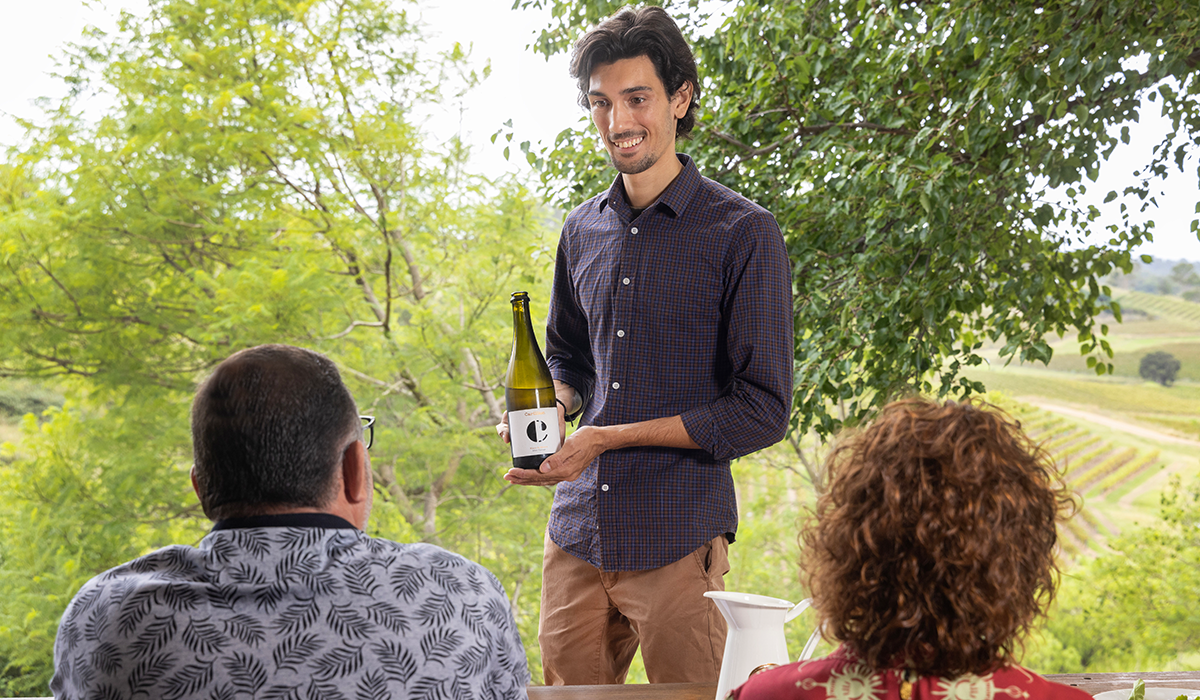 A man holding a bottle of Carillion wine and speaking to cellar door guests