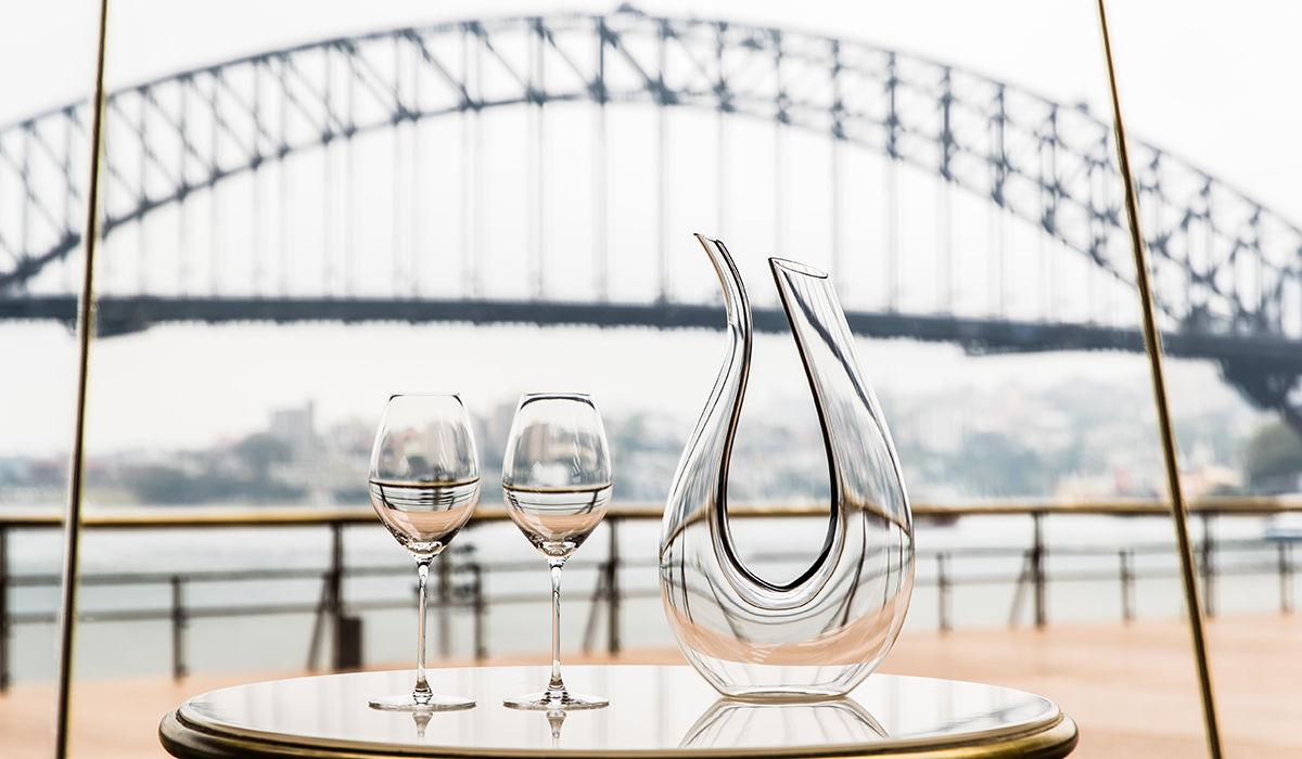 RIEDEL Amadeo decanter and two glasses on a table with the Sydney Harbour Bridge in the background.