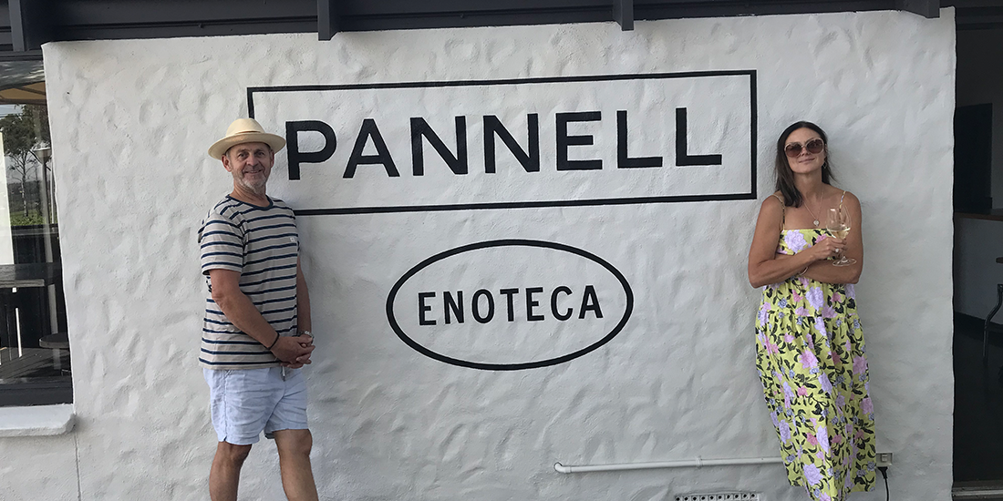 Steve and Fi standing outside the Pannell Enoteca cellar door, they're leaning against a wall with Pannell Enoteca written in black.